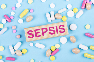 On a blue background, multi-colored pills and a wooden block with the text SEPSIS. View from above....
