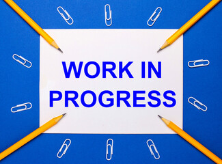 On a blue background, white paper clips, yellow pencils and a white sheet of paper with the text WORK IN PROGRESS