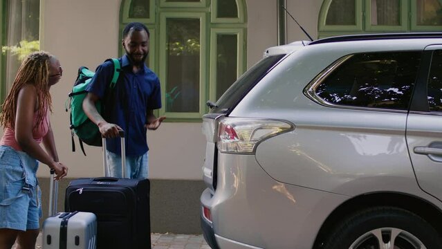 African american couple loading voyage luggage in car while getting ready for summer citybreak departure. Boyfriend and girlfriend putting baggage and trolleys in vehicle trunk.