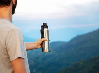 Naklejka premium Man hiking in mountains, break point to have rest and drink water using thermo mug, zero waste concept