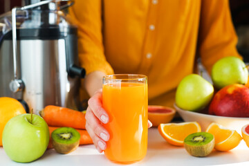 A woman's hand holds a glass of freshly made natural multifruit juice. Healthy and tasty juices at home. Using a juicer. Close-up. Selective focus.