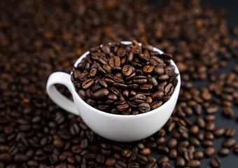 Close up of a fragrant coffee beans in a white cup on a coffee beans on a black background. Selective focus.