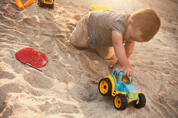 Child playing with toys in sandbox. Little boy having fun on playground in sandpit. Outdoor creative activities for kids. Summer and childhood concept