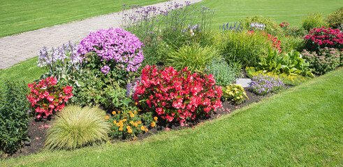 colorful flower bed in the park with summer flowers, walkway and green lawn