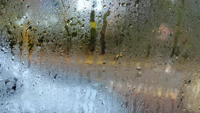 Inside a car after it rained, looking at the window glass covered with water condensation; blurry confused surface, with a random passerby moving on the background.
