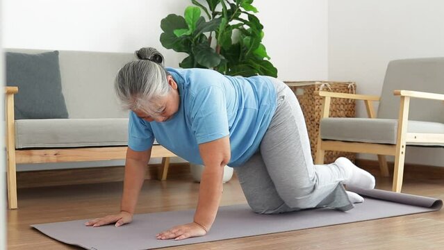 Asian elderly woman exercising at home Do a kneeling pose with your legs extended behind you. Social distancing. Health care of the elderly. sports concept