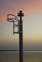 A small metal lighthouse in the village harbor during sunset