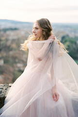 Fototapeta na wymiar Bride in a dress with a cape sits on a stone wall. Bergamo, Italy