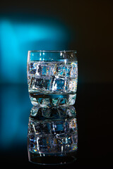 A glass with ice water and ice cubes on a blurred blue background. A refreshing and chilling drink in hot weather.