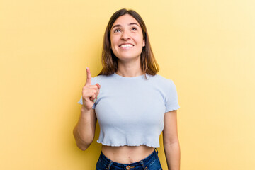 Young caucasian woman isolated on yellow background indicates with both fore fingers up showing a...