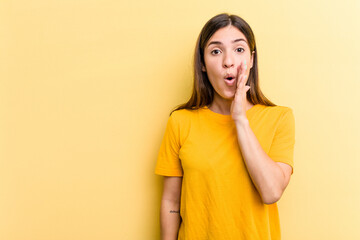 Young caucasian woman isolated on yellow background is saying a secret hot braking news and looking aside