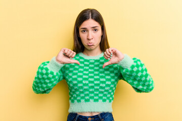 Young caucasian woman isolated on yellow background showing a dislike gesture, thumbs down....