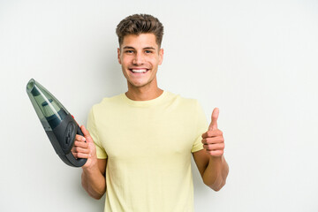 Young caucasian man holding a hand vacuum cleaner isolated on white background smiling and raising thumb up - obrazy, fototapety, plakaty
