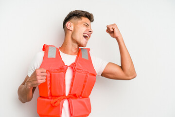 Young caucasian man wearing life jacket isolated on white background raising fist after a victory,...