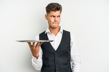 Young caucasian waitress man holding a tray isolated on white background confused, feels doubtful and unsure.