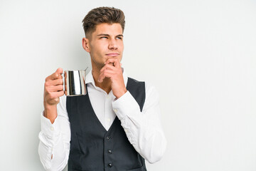 Young caucasian barista man isolated on yellow background looking sideways with doubtful and skeptical expression.