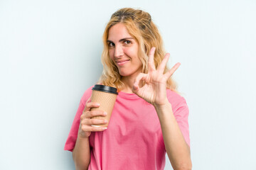 Young caucasian woman holding a take away coffee isolated on blue background cheerful and confident showing ok gesture.