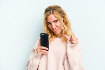 Fototapeta premium Young caucasian woman holding mobile phone isolated on blue background feels proud and self confident, example to follow.