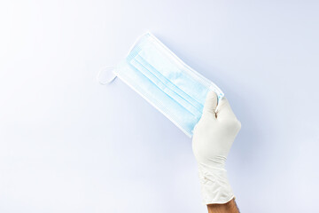 a male hand in a white medical glove holds a medical mask.  On a white background.  Lots of empty space