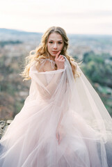Fototapeta na wymiar Bride in a dress with a cape sits on the wall. Bergamo, Italy