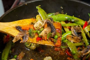 Stewed vegetables with champignon mushrooms and broccoli in a frying pan with a wooden spatula.