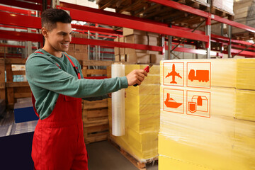 Worker wrapping boxes with shipping icons in stretch film at warehouse