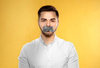 Man with taped mouth on yellow background. Speech censorship - obrazy, fototapety, plakaty