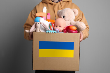 Humanitarian aid for Ukrainian refugees. Man holding donation box full of different toys on grey...