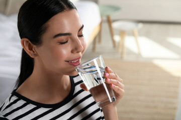 Young woman drinking water indoors, space for text. Refreshing drink