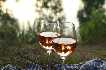 Glasses of delicious rose wine on picnic blanket near lake, closeup