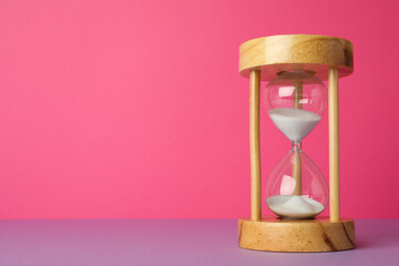 Hourglass with flowing sand on violet table against pink background, space for text. Menopause...