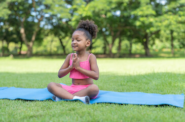 Naklejka na ściany i meble African American little girl sitting with closed eyes practicing meditate yoga on roll mat in the park. Kids afro girl with curly hair engaged training yoga in outdoor.
