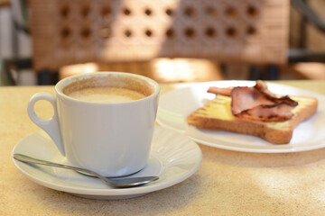 Cup of coffee and delicious sandwich with fried bacon on beige table
