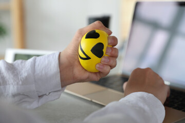 Woman squeezing antistress ball while working on laptop in office, closeup