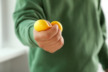 Man squeezing yellow stress ball indoors, closeup