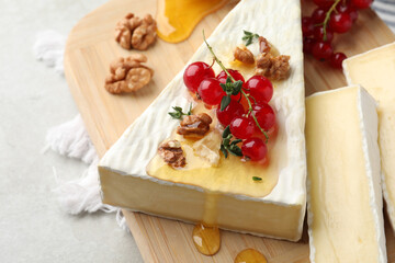 Brie cheese served with red currants, walnuts and honey on light table, closeup