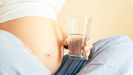 Pregnant water drinking woman. Young pregnancy mother drink water. Pregnant lady waiting of baby. Glass of water. Concept of maternity, expectation.