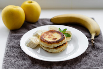 Cottage cheese pancakes with banana and an apple in a white plate. Traditional breakfast or lunch. Traditional Ukrainian breakfast.