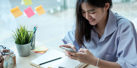 Female student taking notes from a book and using smart phone at home