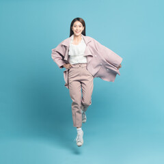 Young beautiful asian woman with smart casual cloth wearing pink coat smiling and jumping isolated on blue background