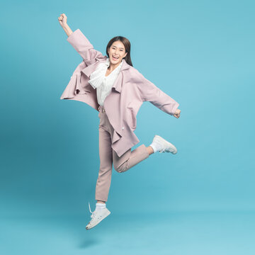 Young beautiful asian woman with smart casual cloth wearing pink coat jumping with excite feeling isolated on blue background