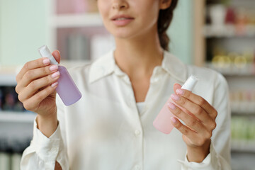 Hands of young shopper holding two plastic bottles with liquid nailcare products in cosmetic shop...