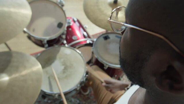 High angle selective focus shot of African American drummer playing drumkit during rehearsal