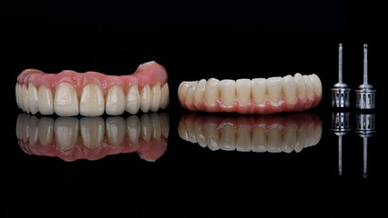 Two ceramic prostheses of the upper and lower jaw with screwdrivers on black glass with reflection