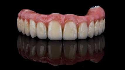 Great dental prosthesis of the upper jaw made of ceramics with a pink gum on a black background with a reflection