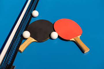 Table tennis rackets and a white plastic ball on a blue background.
