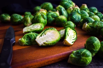 Fotobehang Halved Brussels Sprout Viewed Closeup on a Wood Cutting Board: Fresh brussels sprouts halved with a paring knife on a wooden carving board © Candice Bell