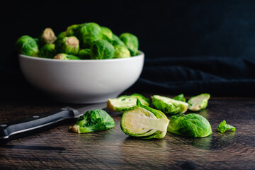 Low Angle View of Halved Brussels Sprouts with a Bowl in the Background: Halving fresh Brussels sprouts on a dark wood background