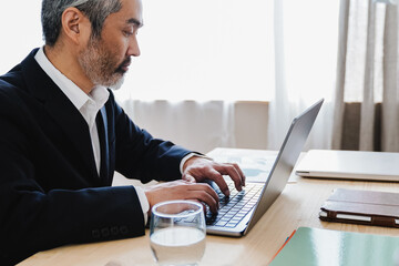 Business senior Asian man working on computer laptop inside bank office - Focus on hands