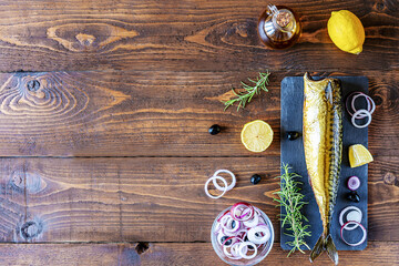 Smoked mackerel on stone cutting board, rings of onion, lemon, olives, olive oil, rosemary over wooden background